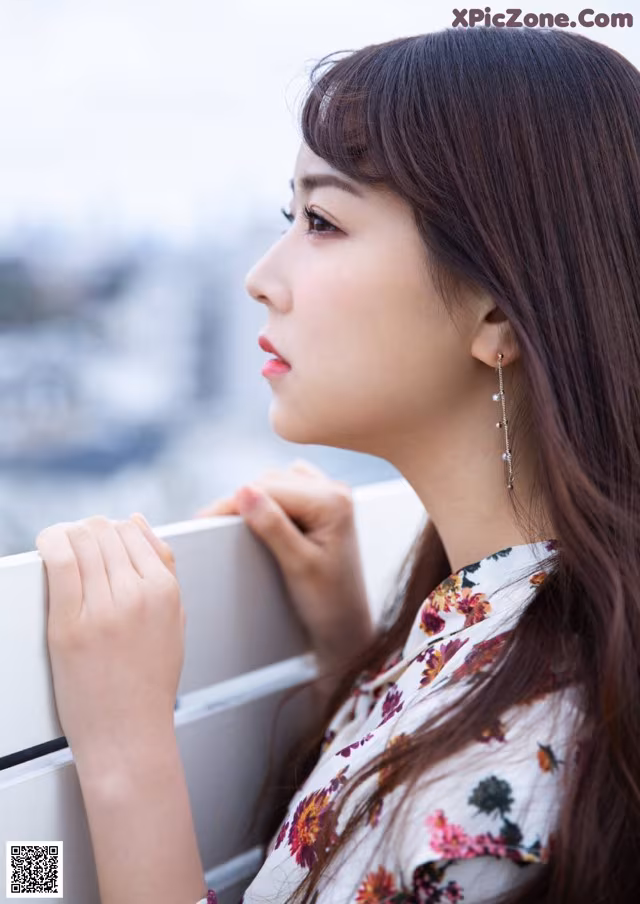 A woman with long brown hair leaning against a railing.