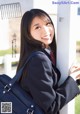 A woman in a school uniform leaning against a pole.