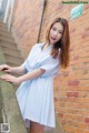 A woman in a blue and white striped dress leaning against a brick wall.